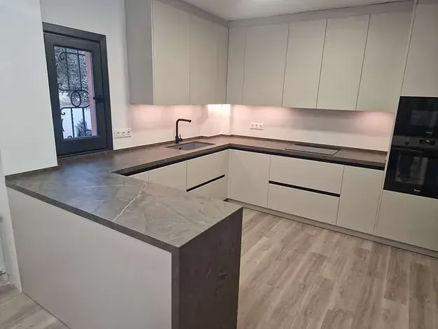 Una cocina con gabinetes blancos y pisos de madera y una ventana.