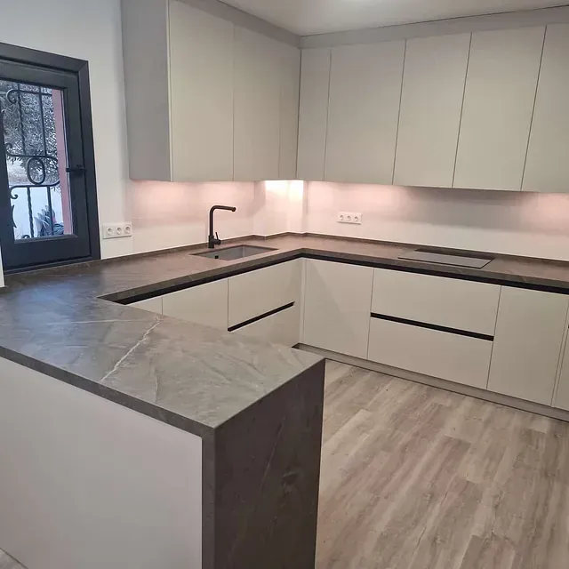 Una cocina con gabinetes blancos, un fregadero y una ventana.