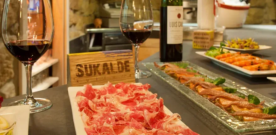 Una botella de vino sukalbe reposa sobre una mesa junto a un plato de carne.