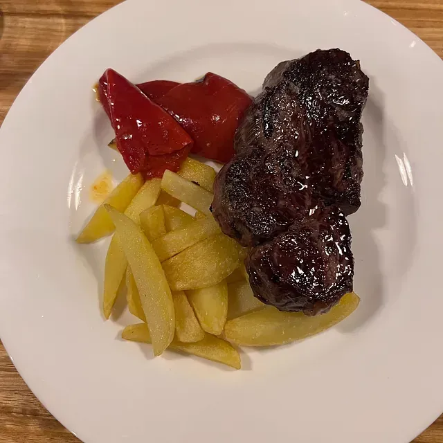 Un plato blanco cubierto con carne y papas fritas.