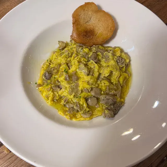 Un plato blanco cubierto con huevos revueltos y un trozo de pan.