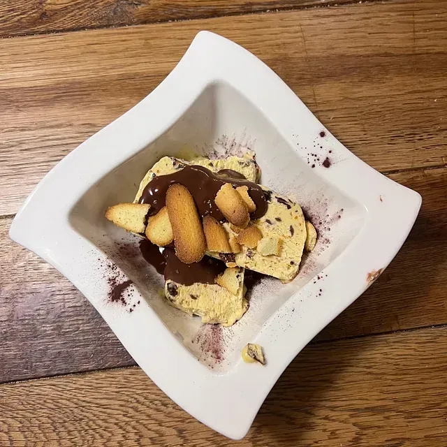 Un tazón blanco lleno de galletas y salsa de chocolate sobre una mesa de madera.