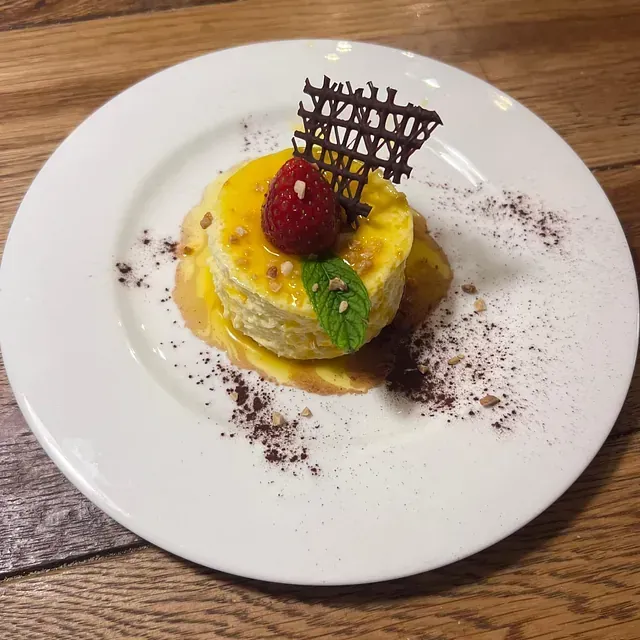 Un plato blanco cubierto con un postre con una frambuesa encima.