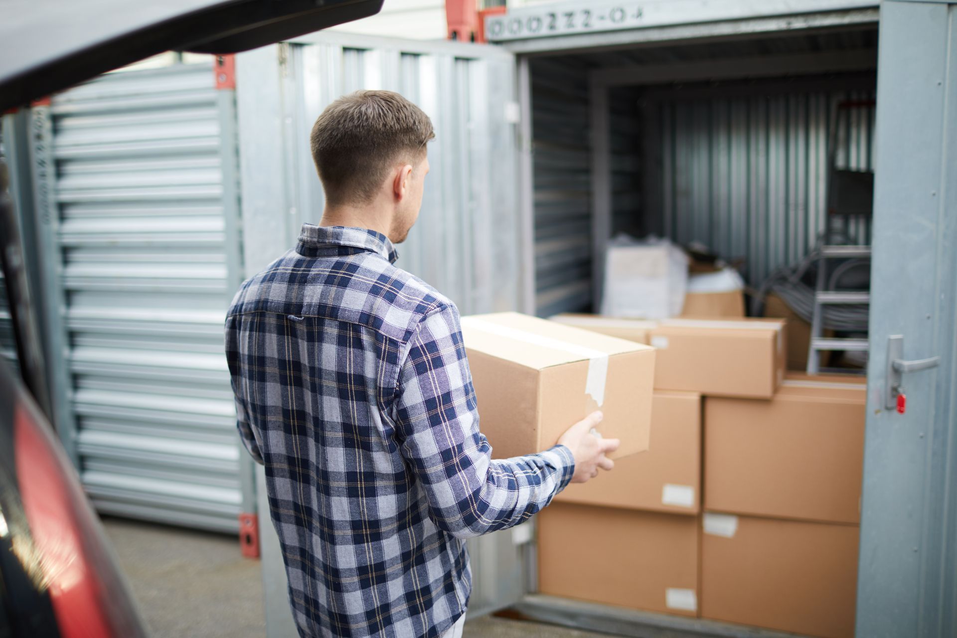 Une personne en chemise à carreaux transporte un carton dans un conteneur de stockage rempli de cartons.