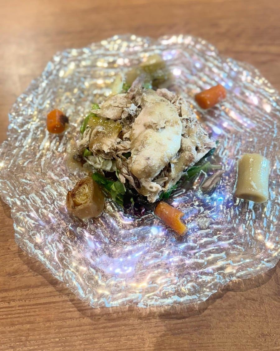 Plato de carne desmenuzada, zanahorias y otras verduras en un plato de vidrio texturizado, sobre una mesa de madera.