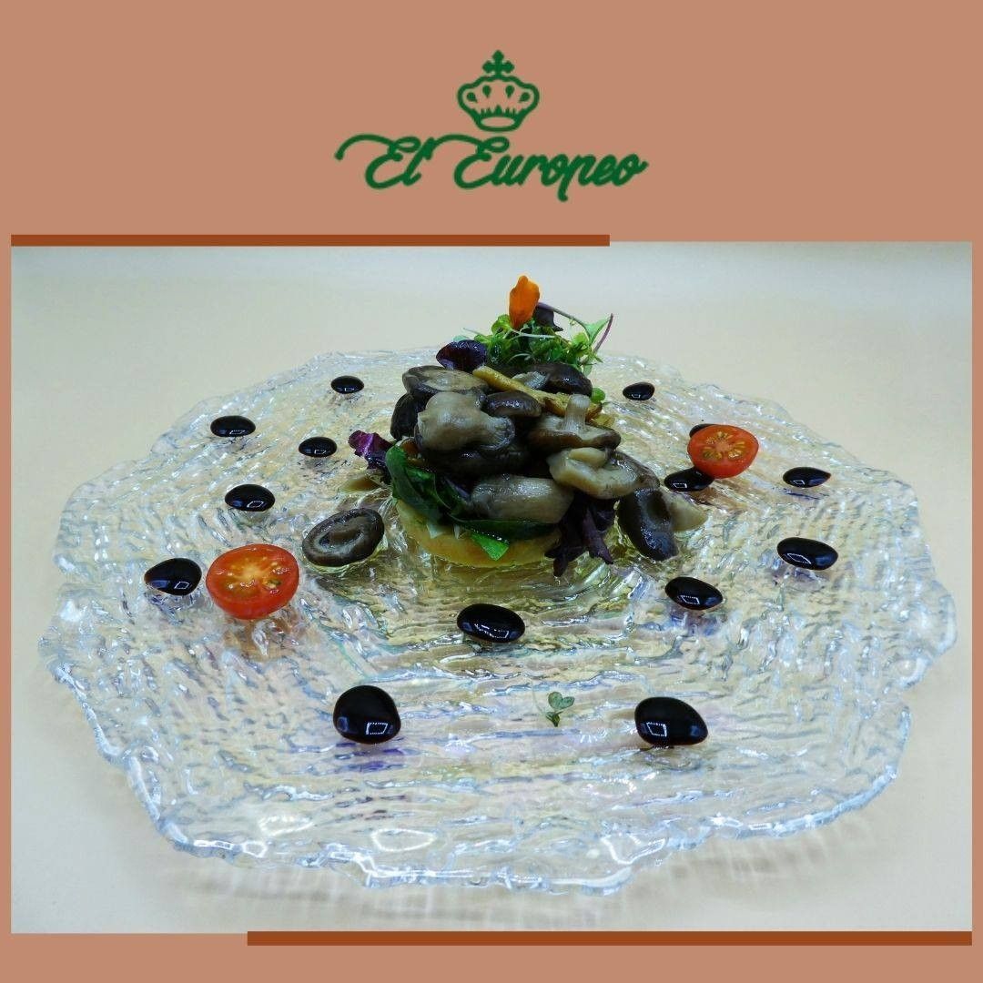 Plato de champiñones, aceitunas y tomates dispuestos artísticamente sobre un plato transparente y texturizado.