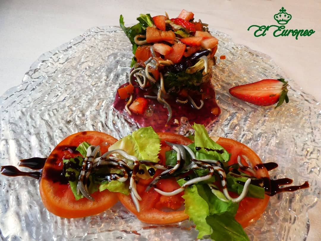 Ensalada con tomates, fresas, verduras y glaseado balsámico en un plato de vidrio texturizado.