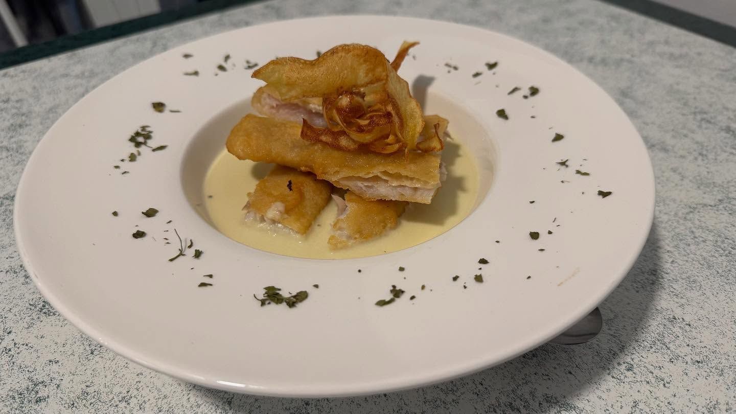 Comida frita en plato con salsa, adornada con hierbas.