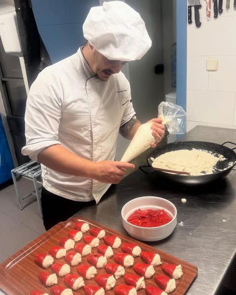 Chef colocando relleno en pimientos rojos, mientras prepara un plato en la cocina.