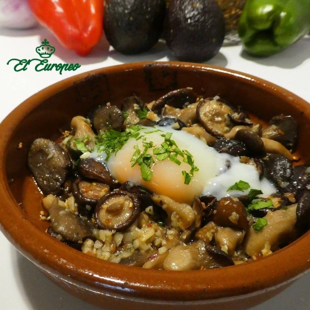 Champiñones, huevo y hierbas en un recipiente de cerámica, con verduras de fondo.