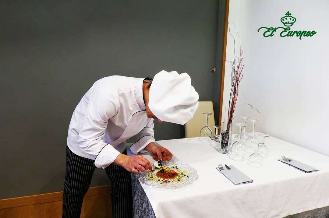 Un chef sirve comida en un plato en una mesa.