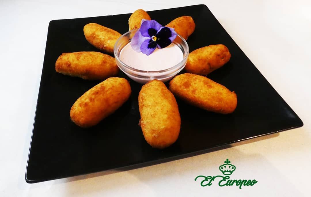 Croquetas doradas dispuestas alrededor de una salsa rosa en un recipiente de cristal.