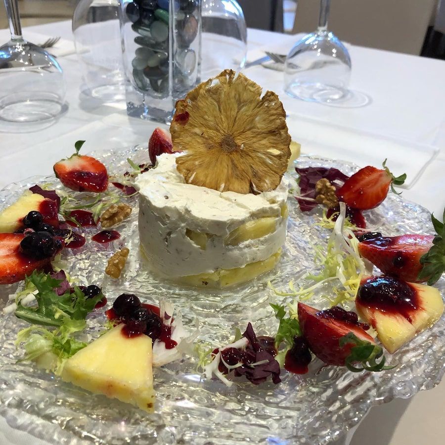 Postre de frutas y crema en plato de vidrio; incluye piña, fresas y nueces.