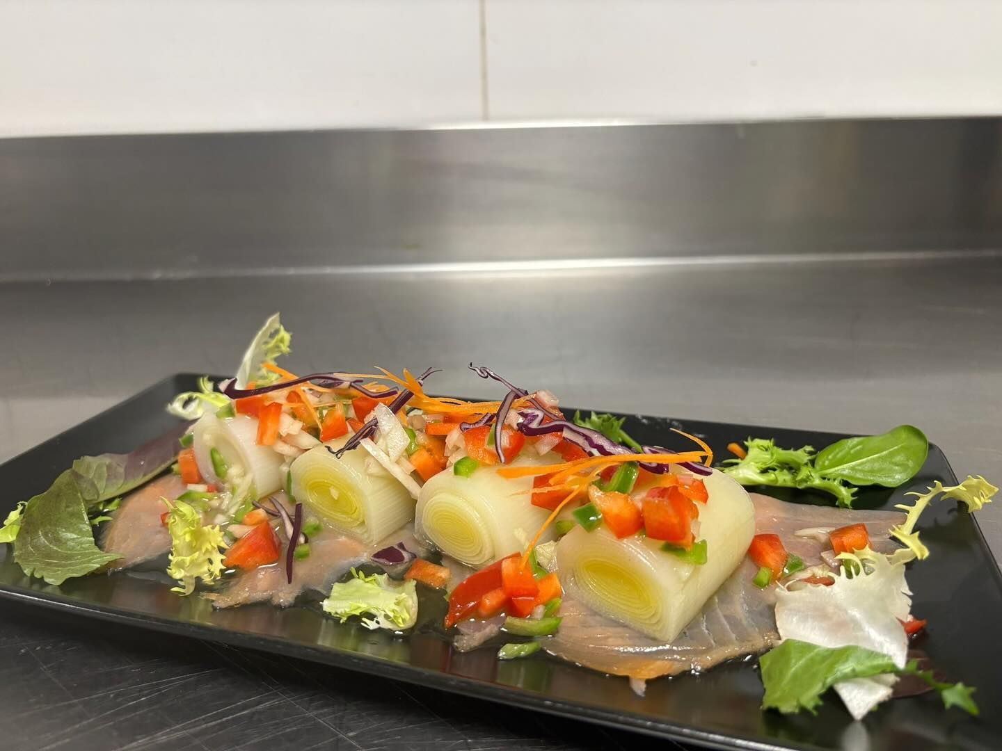 Plato de comida compuesto por rollitos con verduras y pescado, adornado sobre una superficie negra.