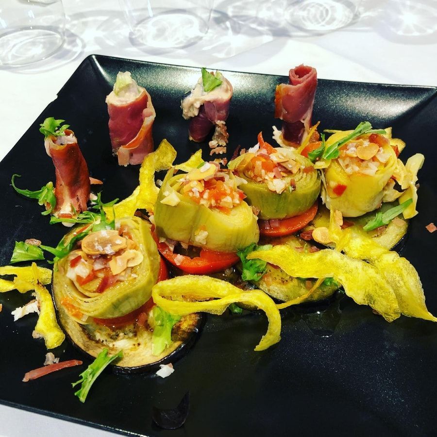 Aperitivos de alcachofa con prosciutto, calabaza frita y berenjena, en plato negro.