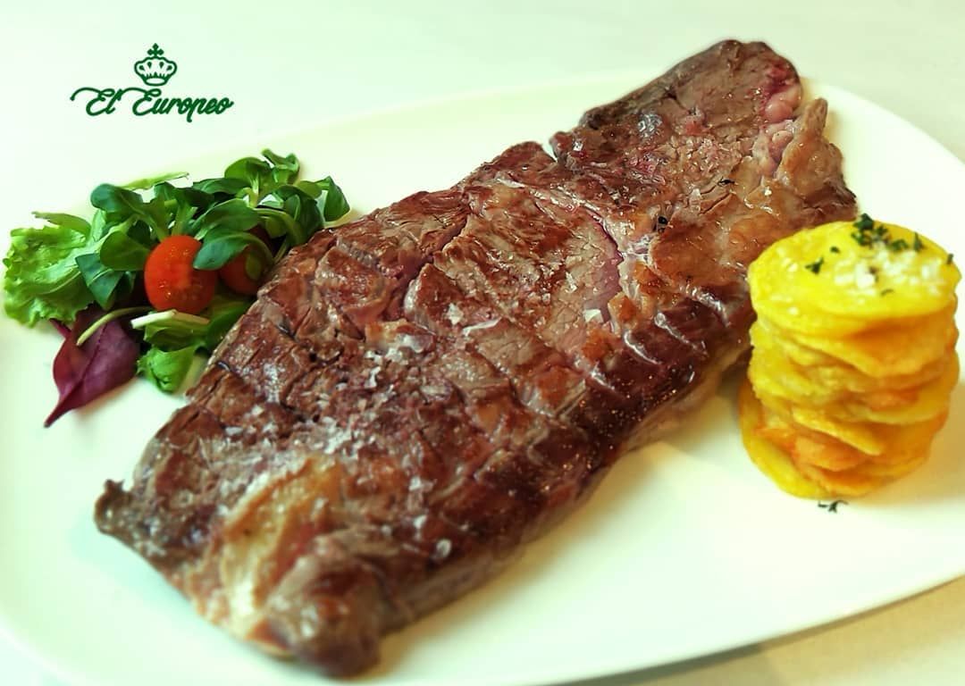 Bistec a la parrilla con pila de patatas fritas y ensalada en un plato blanco.