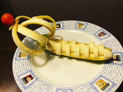 Arte de plátano en un plato con un diseño tejido y pelado. Un tomate cherry reposa sobre las espirales de la cáscara.