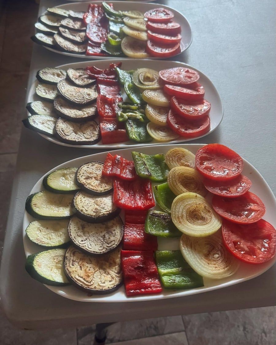 Tres platos ovalados de verduras a la parrilla: calabacín, berenjena, pimientos rojos y verdes, cebollas y tomates.