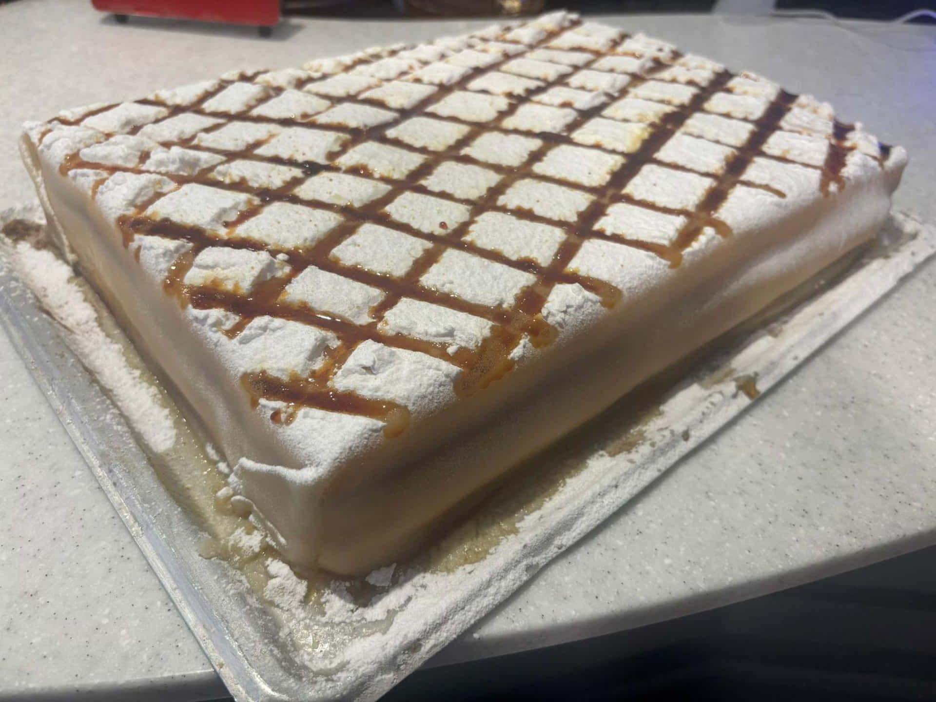 Pastel rectangular con glaseado blanco, enrejado de caramelo y azúcar en polvo sobre una bandeja transparente.