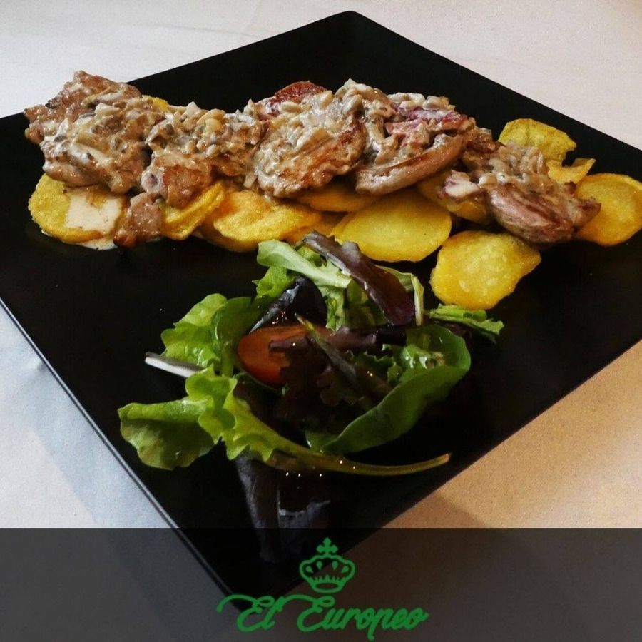 Medallones de cerdo en salsa de crema, patatas fritas y ensalada en plato negro.