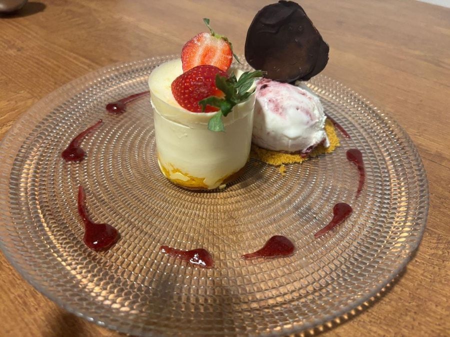 Plato de postre con bizcocho blanco, fresa, helado, pera y salsa roja.