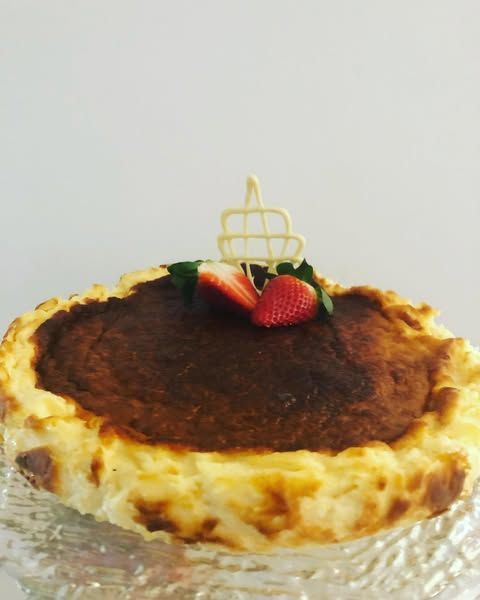 Tarta de queso vasca quemada con fresas y decoración de chocolate blanco sobre plato de cristal.