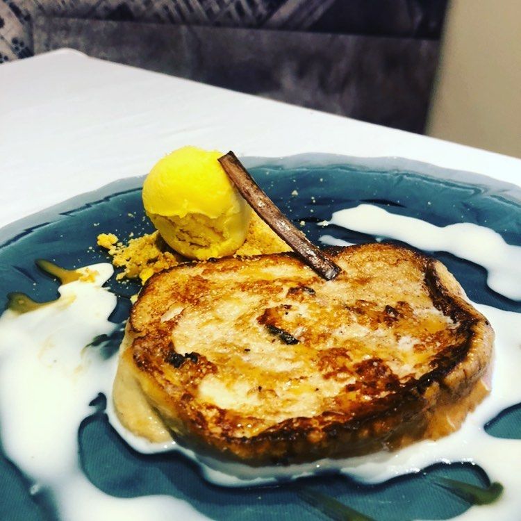 Postre de tostada francesa con helado y rama de canela, servido en un plato azul.