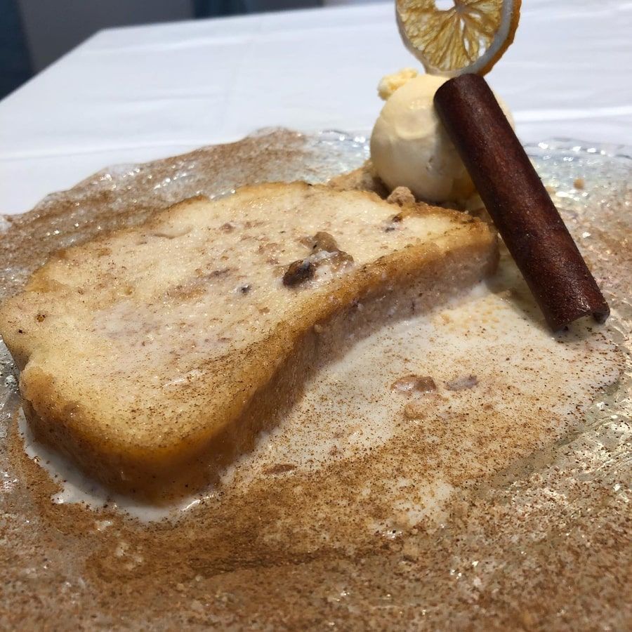 Postre de budín de pan con helado, rama de canela y rodaja de limón.