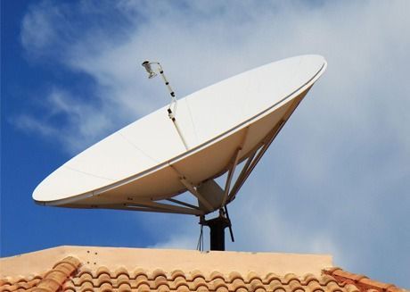 Una gran antena parabólica blanca sobre un tejado de tejas