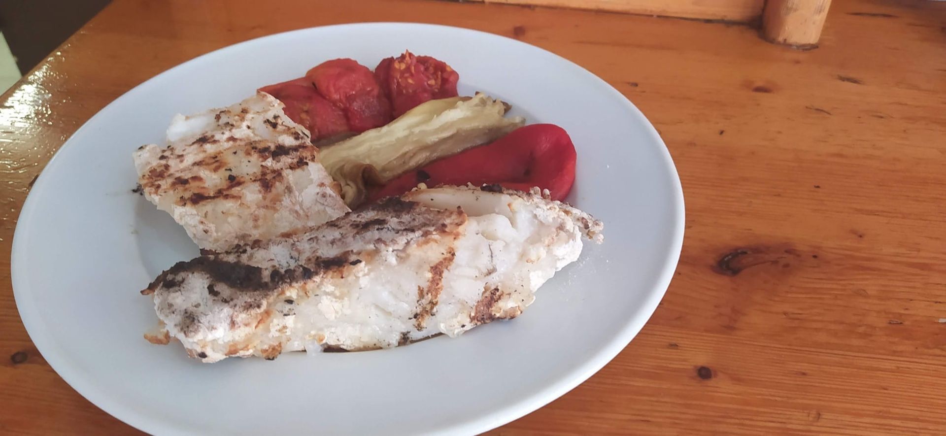 Un plato blanco cubierto con carne y verduras sobre una mesa de madera.