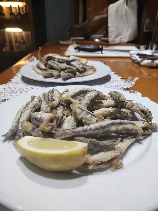Un plato de pescado frito con una rodaja de limón sobre una mesa.