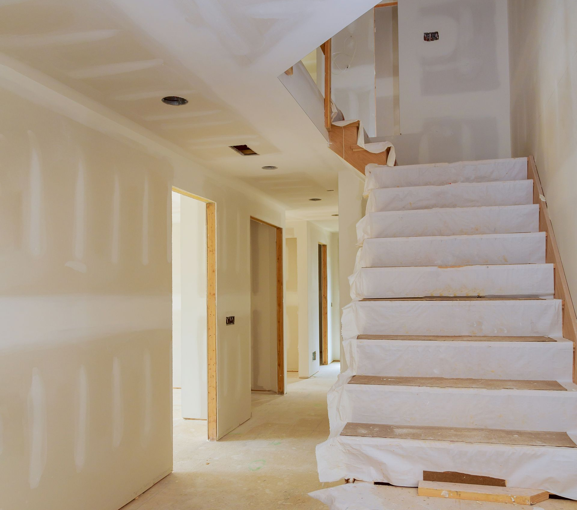 Couloir intérieur et escalier en construction ; cloisons sèches, bois brut et bâches de protection.
