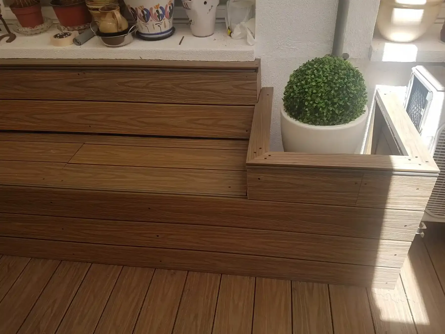 Banco de madera con jardinera incorporada que contiene un topiario, sobre un piso de madera.