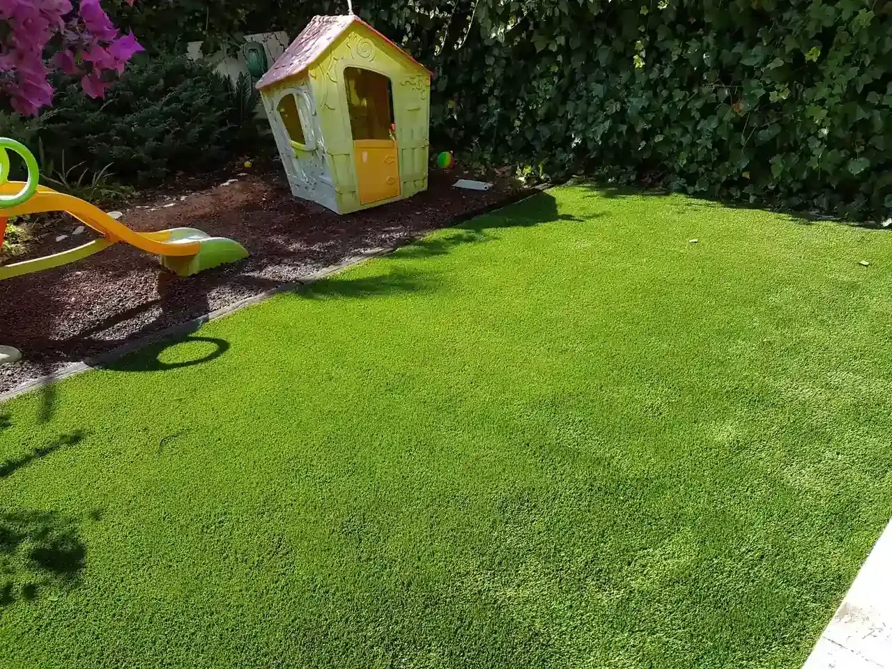 Césped artificial verde con casita de juegos y tobogán en un jardín.