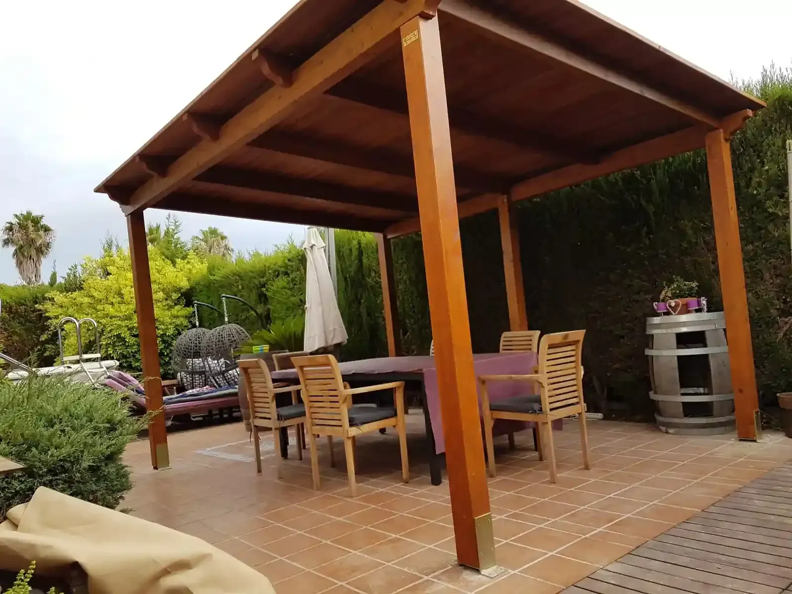 Pérgola de madera sobre un patio con mesa y sillas, cerca de un jardín.