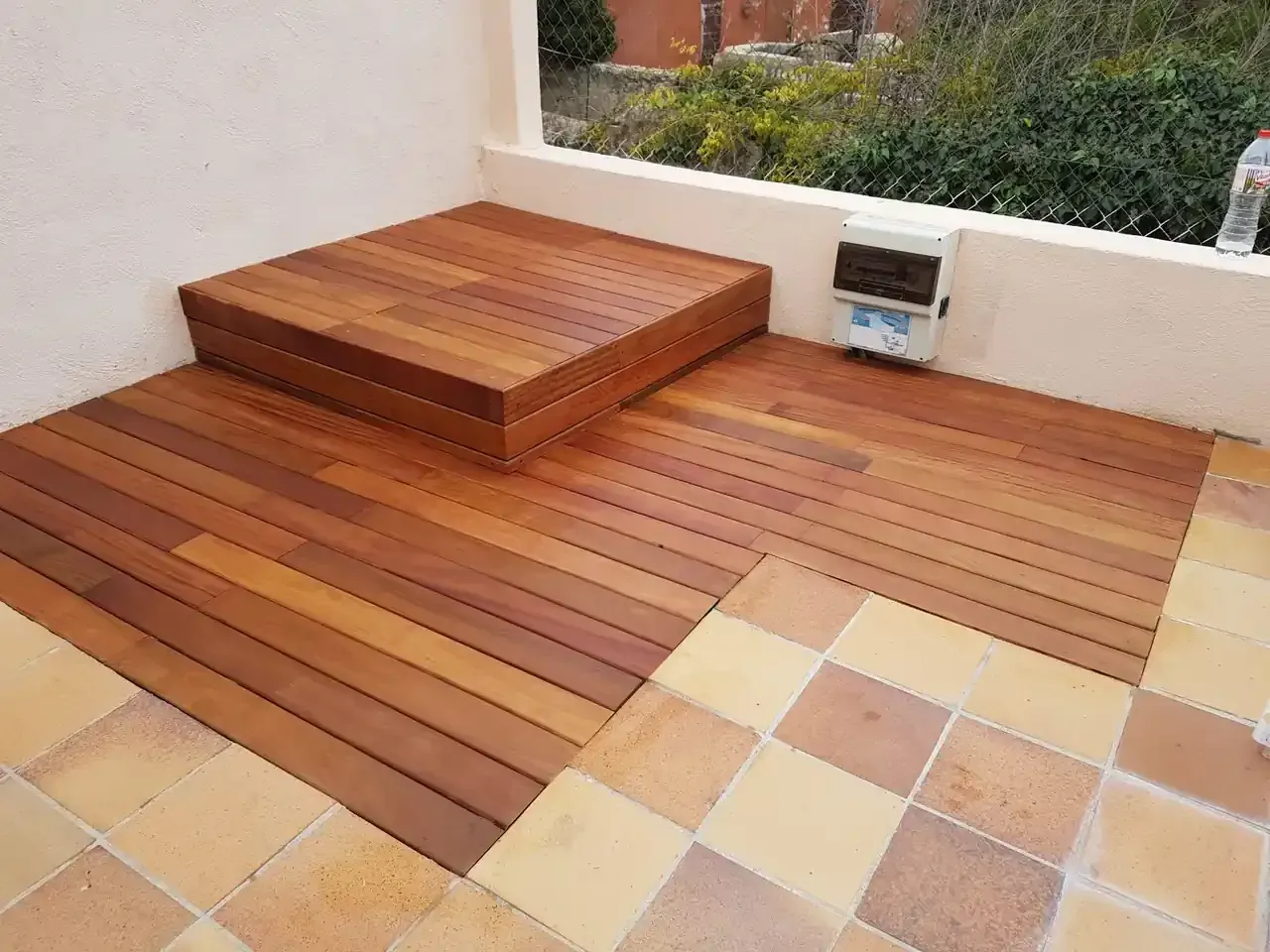 Deck de madera con escalón y patio de baldosas de terracota.