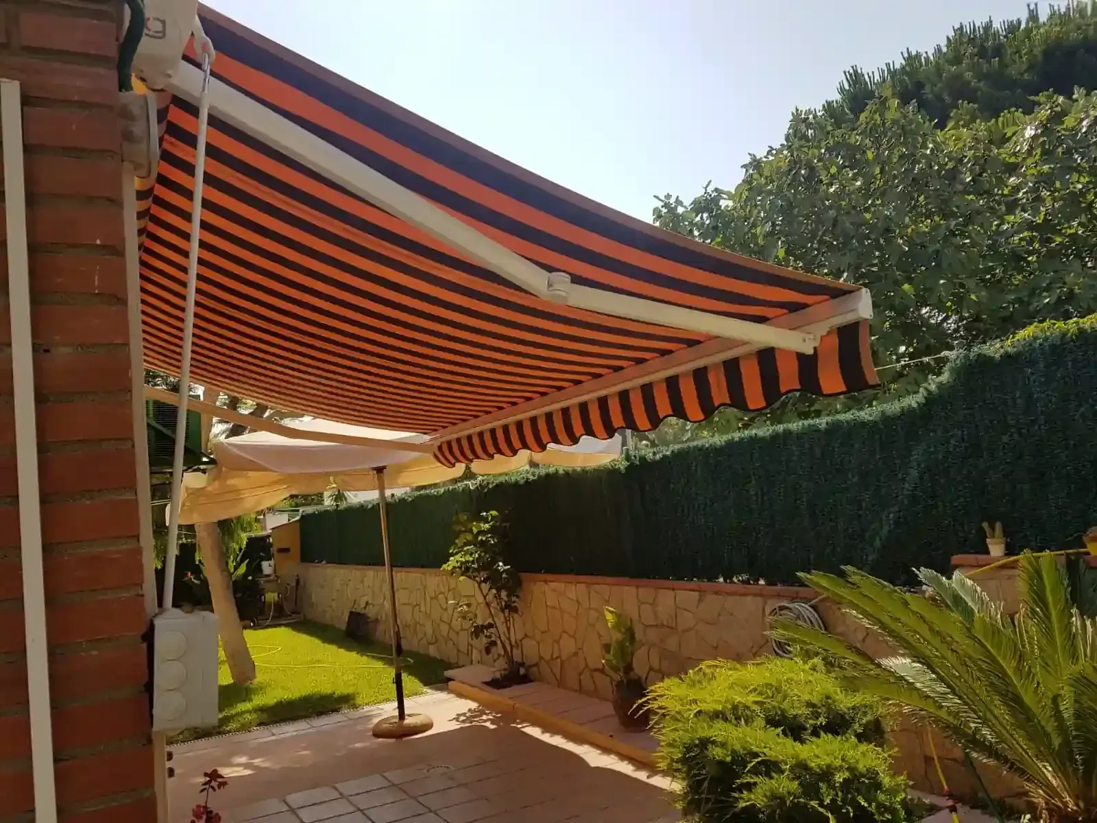 Toldo de rayas naranjas y negras sobre un patio en un jardín trasero soleado.