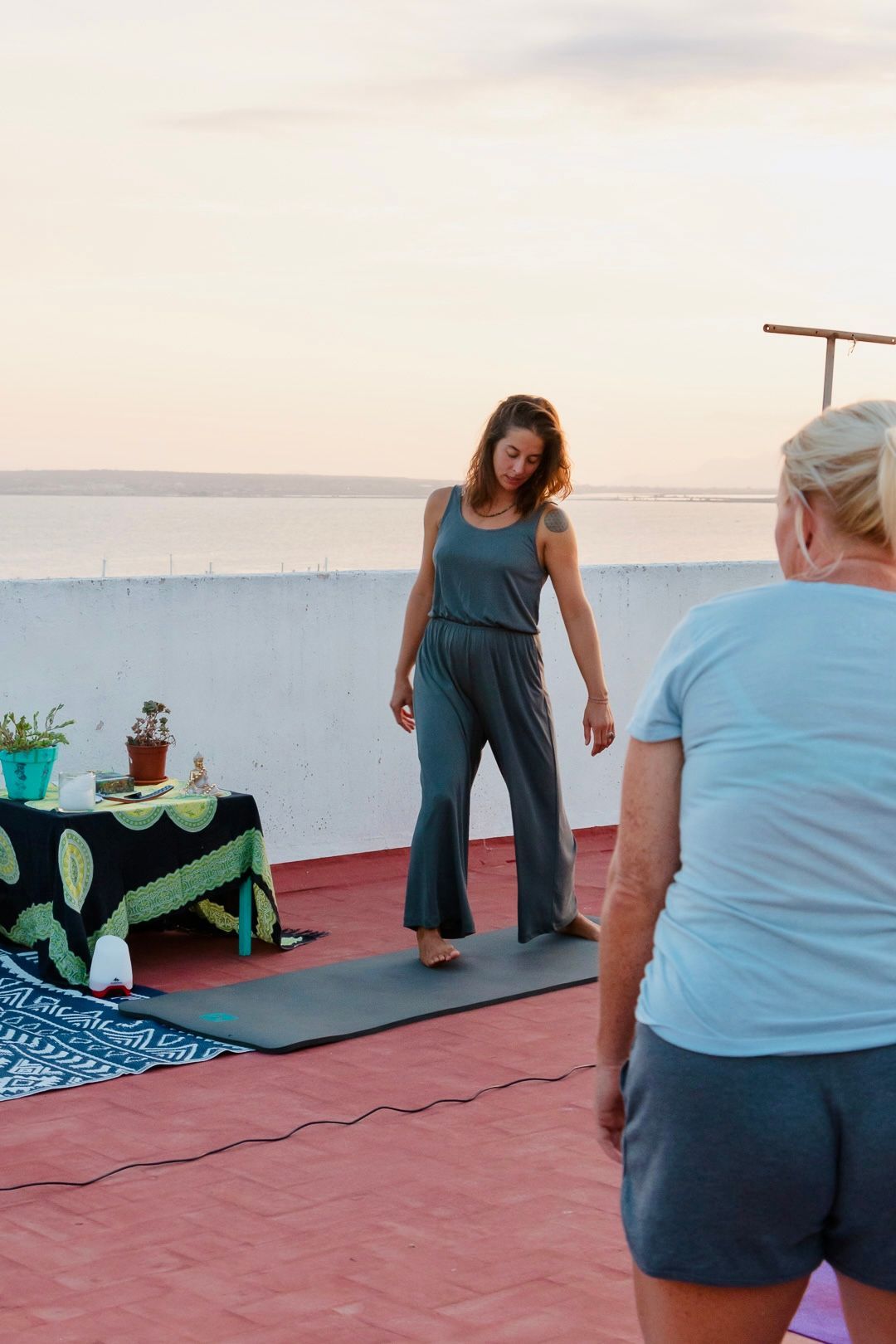 Una mujer está parada sobre una estera de yoga mientras otra mujer la observa.