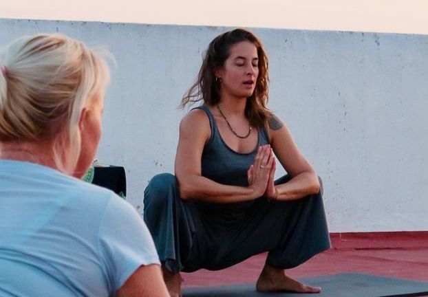 Una mujer está en cuclillas sobre una esterilla de yoga mientras otra mujer observa.