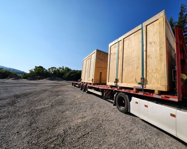 Sur un chantier, camion avec remorque et deux grosses caisses en bois