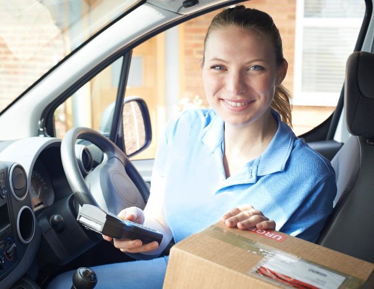 Una mujer está sentada en un coche sosteniendo una caja y un portapapeles.