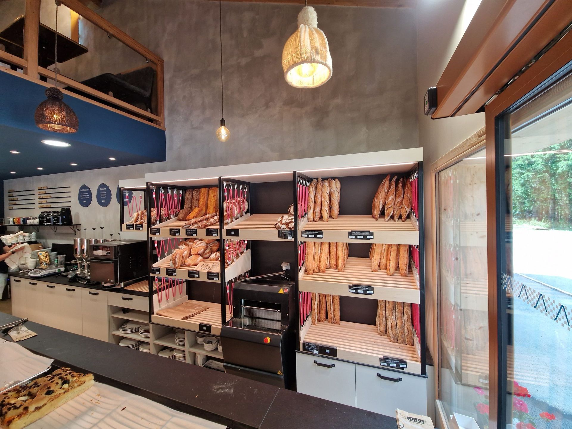 Intérieur d'une boulangerie avec présentoirs à pain, un comptoir avec des pâtisseries et des suspensions lumineuses.