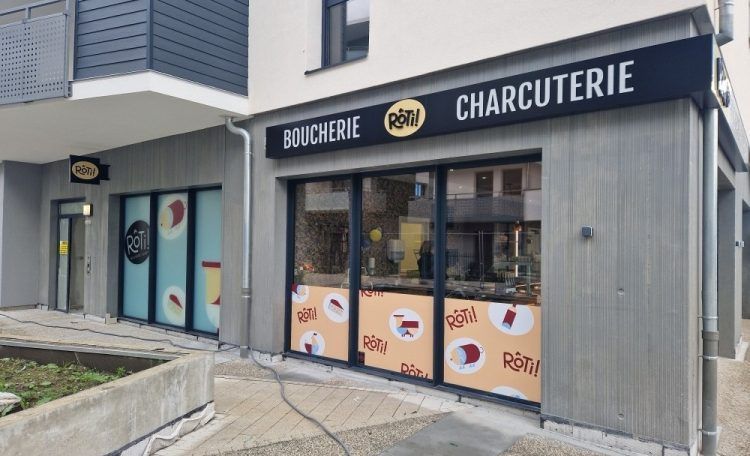 Extérieur de boucherie, façade grise, grandes fenêtres, enseigne indiquant Boucherie Charcuterie.