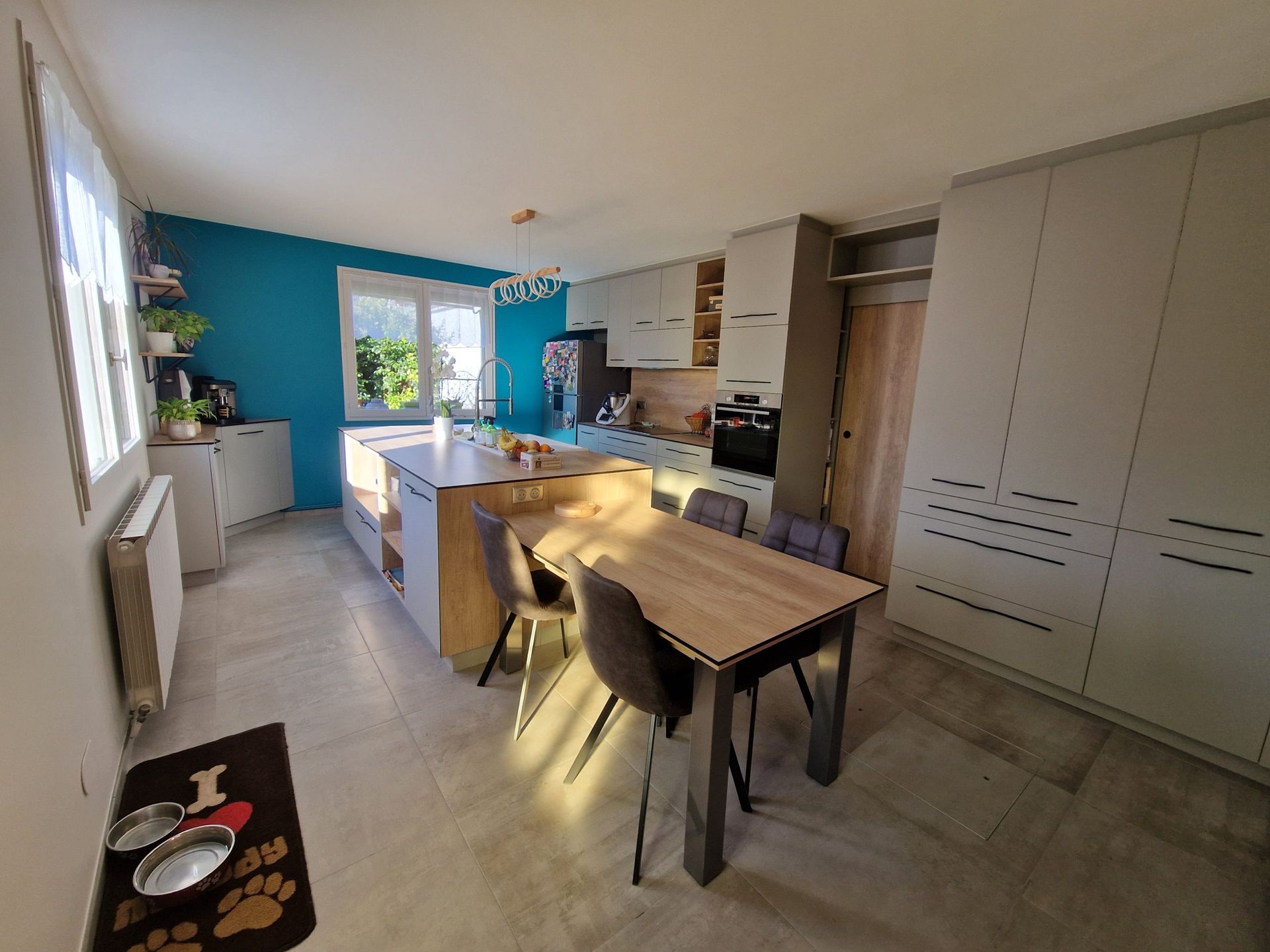 Cuisine moderne avec mur bleu sarcelle, îlot en bois clair et table en bois foncé.