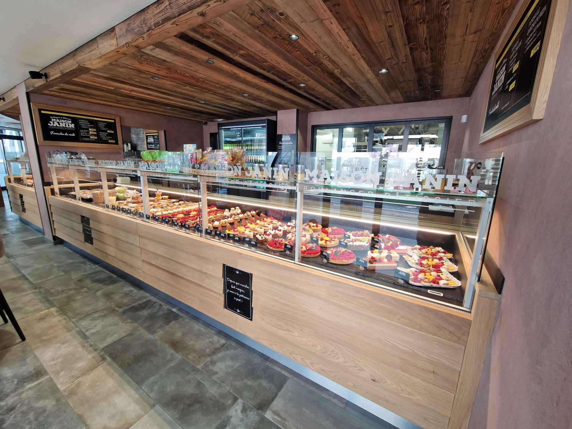 Vitrine de boulangerie avec pâtisseries et gâteaux, éléments en bois, sol en pierre.