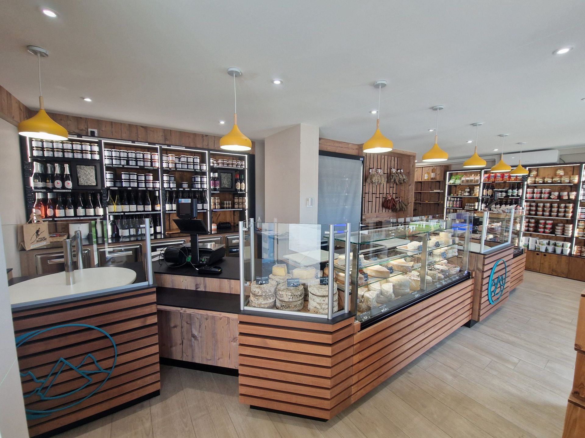 Intérieur d'une fromagerie-épicerie fine avec vitrines, étagères de produits et suspensions lumineuses jaunes.