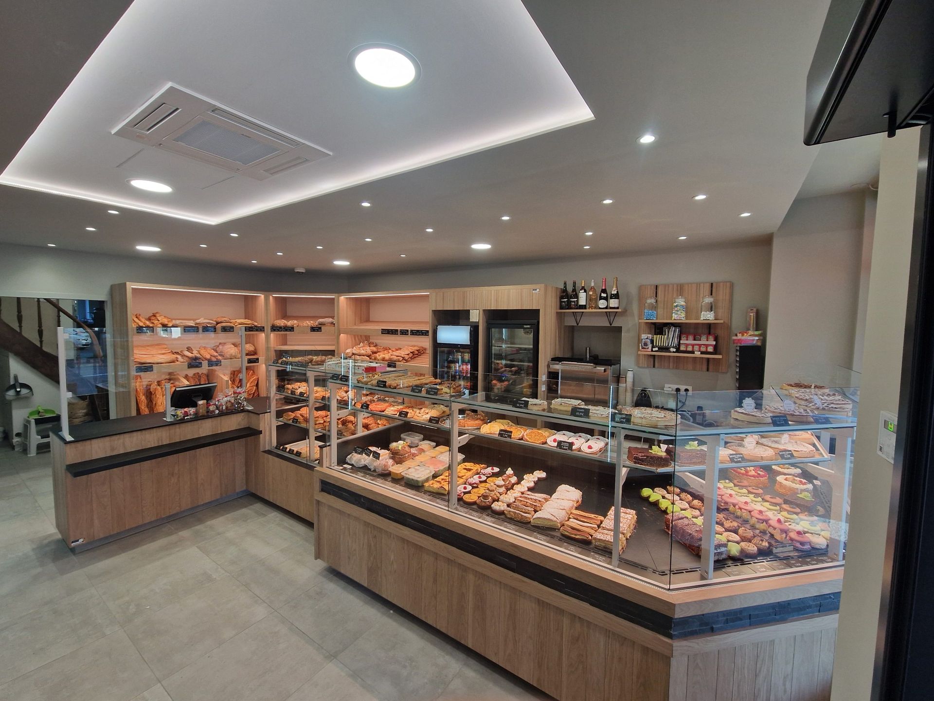 Intérieur de boulangerie avec des produits de boulangerie exposés dans des vitrines, des comptoirs en bois clair et un éclairage zénithal.