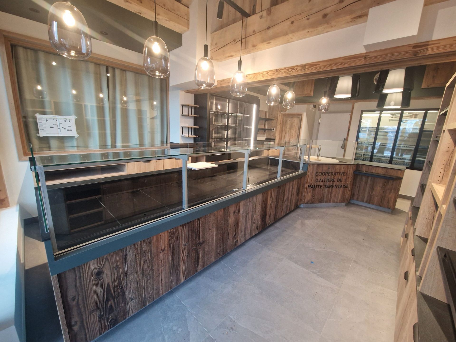 Espace commercial vide avec comptoir en bois, vitrines et suspensions lumineuses.