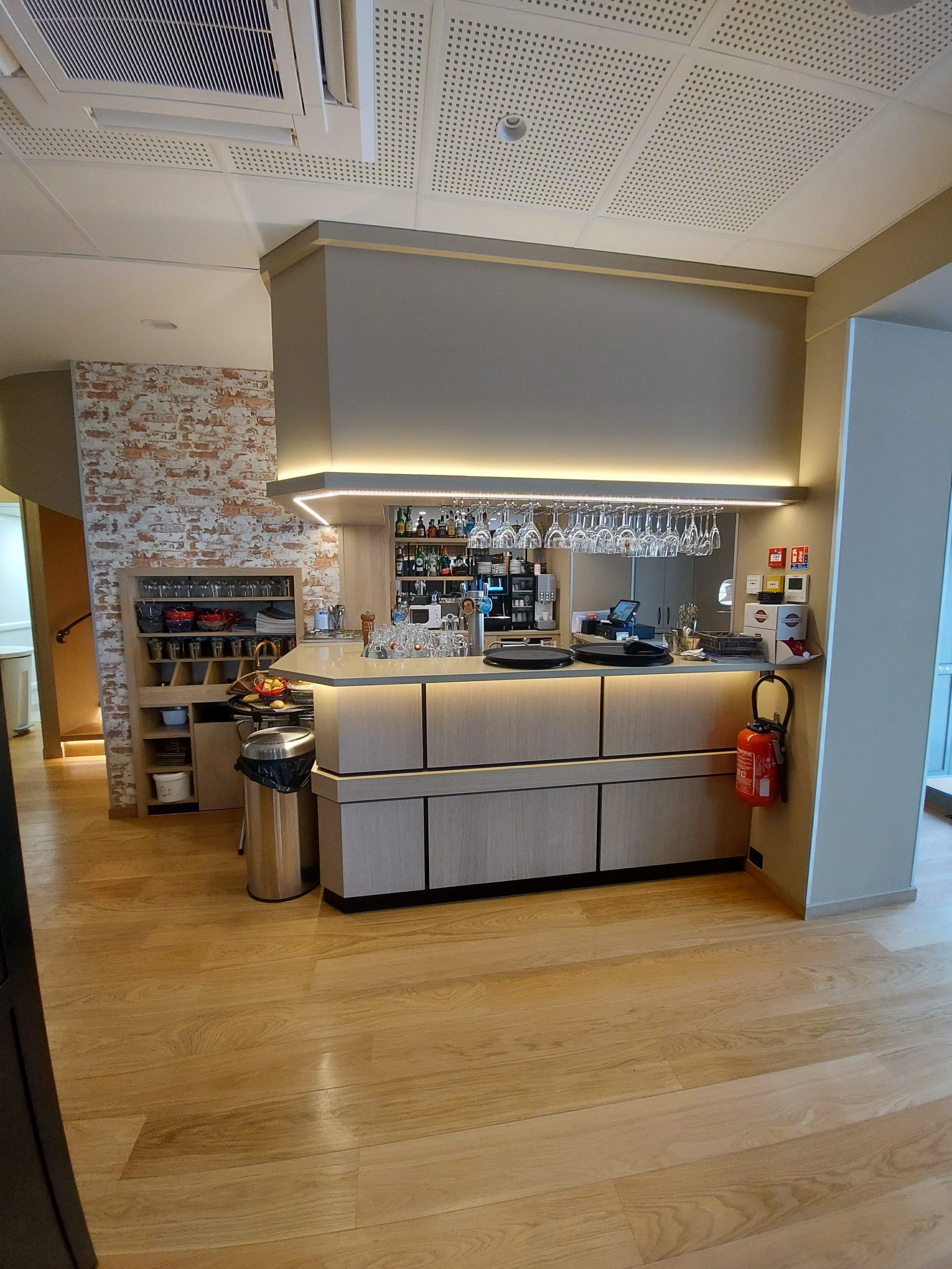 Bar avec parquet, comptoirs et luminaires décoratifs au plafond. Un mur de briques et des verres suspendus ornent le plafond.