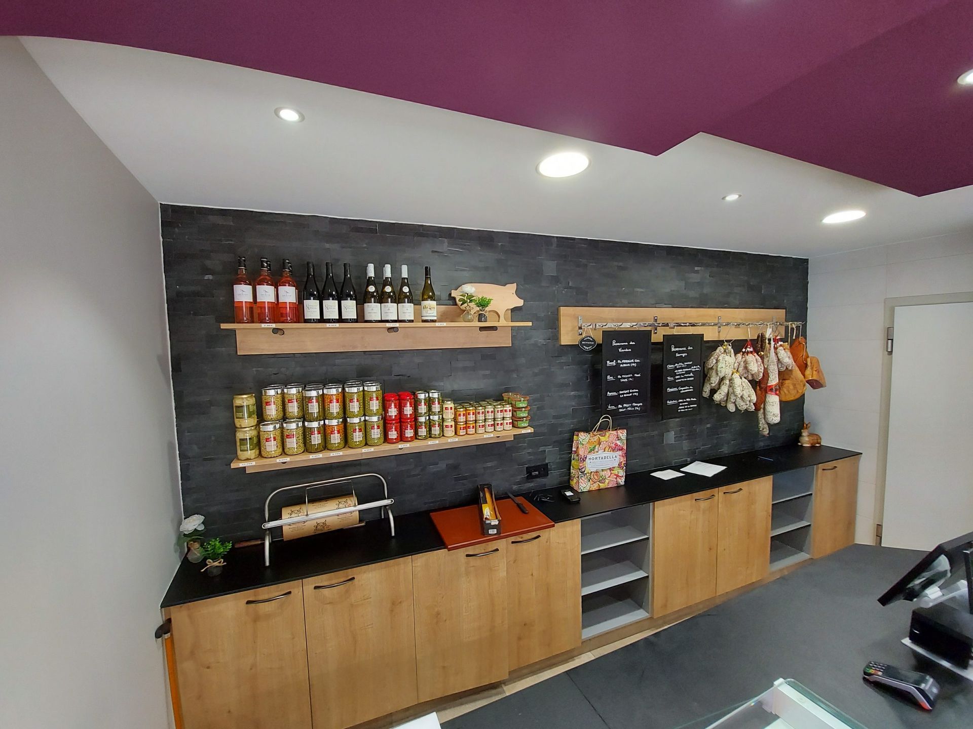 Des étagères garnies de produits alimentaires dans un magasin, avec des éléments en bois et en ardoise sombre, et un plafond violet.